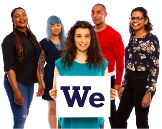 A woman standing in front of a group of people. She is holding up a sign that says 'We'.